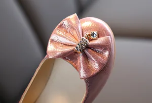 Close-up of sparkling pink girls shoes featuring a rhinestone bow and diamond pendant