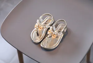 Detalle de sandalias champagne para niña con perlas, lazo de satén y suela metalizada