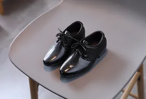 Detailansicht der schwarzen Jungen-Lacklederschuhe mit Schlangenhaut-Struktur und Schnürung