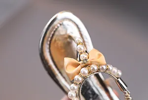 Vista macro de sandalias doradas para niña con perlas y detalle de lazo satinado