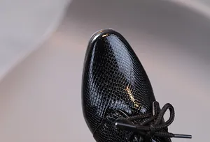 Makroaufnahme schwarzer Lackleder-Jungenschuhe mit geprägter Schlangentextur und Schnürsenkeln