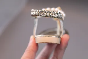 Detalle de sandalias doradas para niña con perlas y correa de talón elástica