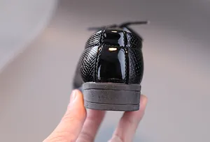 Detail der Jungenschuhe aus schwarzem Lackleder mit Schuppenmuster und Gummisohle