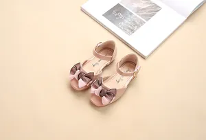 Dettaglio di scarpe Mary Jane rosa con grande fiocco di raso e ciondolo a cuore dorato