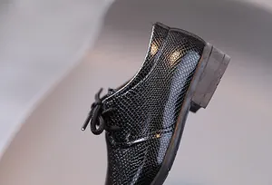 Detail der Jungen-Halbschuhe aus schwarzem Leder mit Echsenstruktur und Holzmaserung