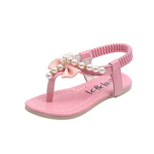 Sandalias rosas para niñas con cuentas y lazo sobre fondo blanco en vista frontal