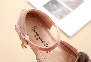 Dettaglio di scarpe da bambina in vernice rosa con fibbia dorata e ciondolo gemma