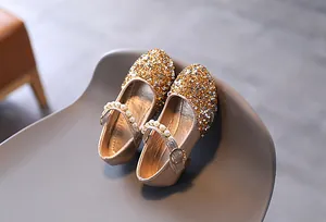 Dettaglio di scarpe Mary Jane dorate con paillettes scintillanti e cinturino di perle