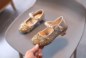 Dettaglio di scarpe da principessa dorate con paillettes e cinturino di perle bianche