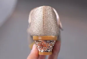Dettaglio di scarpe da bambina con tacco basso, glitter dorati e finitura lucida