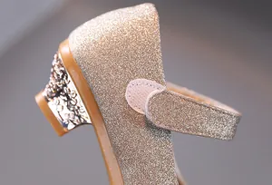 Dettaglio macro di scarpe da bambina con paillettes oro, tacco floreale e velcro