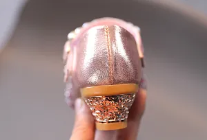Dettaglio di scarpe rosa dorate da bambina con perle e decorazione floreale incisa sul tacco