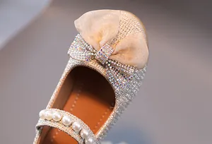 Détail de chaussure princesse dorée pour fille avec nœud pailleté et bride perle