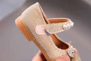 Détail de ballerines pailletées dorées avec nœud en résille et quatre perles décoratives