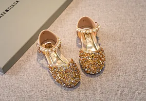 Detail von Mädchenschuhen mit goldener Paillette, Perlenriemen und Metallschnalle