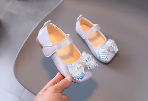 Détail du nœud à paillettes irisées et du strass sur une chaussure pour petite fille