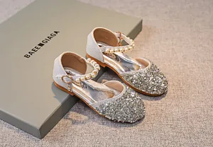 Detail der silbernen Pailletten-Mary-Janes für Mädchen mit Perlenriemen und Herzanhänger
