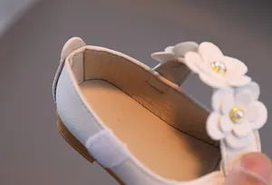Detailaufnahme weißer Mary Jane Schuh mit Blumenriemen, Perle in der Mitte und Goldakzenten