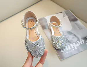 Détail de chaussures de princesse argentées à paillettes avec un grand nœud en cristal