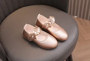 Detailaufnahme goldener Mädchen-Mary-Janes mit 3D-Lederblumen und Perlenverzierung