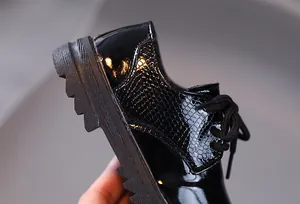 Macro detail of glossy black patent leather and textured snakeskin pattern on boy shoe