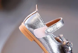 Détail de Mary Janes argentées pour filles avec nœud pailleté et texture métallique