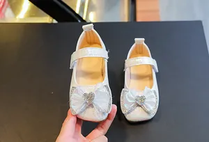 Detail view of white girls Mary Jane shoes featuring a rhinestone bow and glossy finish