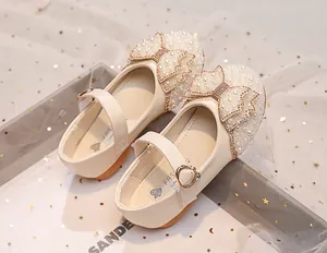 Close-up of girls' dress shoes featuring a pearl and rhinestone bow on cream patent leather