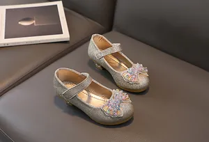 Detail of champagne gold girls' princess shoes with beaded bow on a leather sofa