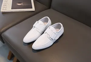 Dettaglio di scarpe in pelle bianca per bambini con fibbia su sfondo grigio testurizzato