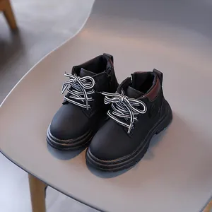 Classic black kids' combat boots with matte finish and striped laces on a grey chair