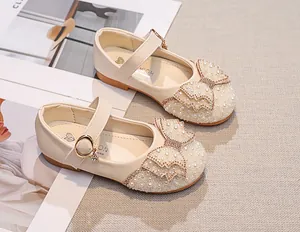 Detail of girls beige Mary Jane shoes with pearls, rhinestones and bow on textured background