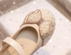 Close-up of sparkling bow with pearls and rhinestones on beige girls princess shoes