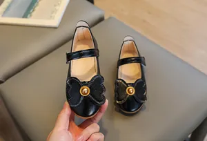 Detail of girl's black patent leather Mary Jane shoes with large bow and gold ornament