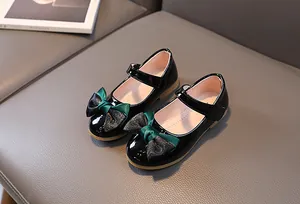 Close-up of black patent leather Mary Jane shoes with ribbon bow and velcro strap detail