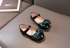 Close-up of black patent leather Mary Jane shoes with bicolored bow on a grey texture