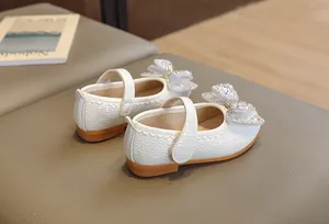 Dettaglio di scarpe Mary Jane bianche da bambina con fiocco di strass e trama intrecciata