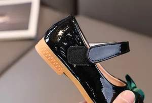 Detail of girls black patent Mary Janes with dark green ribbon bow and gum sole