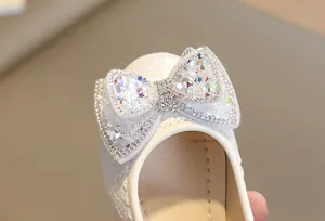 Dettaglio di scarpa bianca in pelle verniciata con fiocco in tulle, paillette e strass lucidi