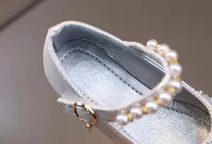 Detailed macro view of silver Mary Jane shoe featuring pearl strap and golden buckle