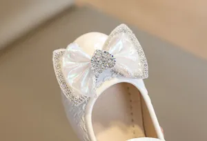 Close-up of girls white princess shoe with woven texture and rhinestone bow detail