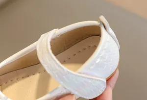 Detail of white girls' Mary Jane shoe showing pearlescent square embossed strap and stitching