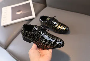 Detail von formellen Jungenschuhen aus schwarzem und goldenem Lackleder mit Karomuster