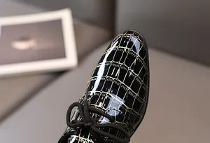 Detail der Jungenschuhe aus schwarzem und goldenem Lackleder mit Kroko-Prägung für Jungen