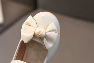 Detail van crème meisjesschoenen met parelglans en een geribbelde strik van lint