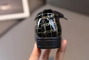 Detailansicht der schwarzen Jungen-Lackschuhe mit goldenem Krokodilmuster an der Ferse