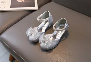 Detail of silver glitter girls princess shoes with bow and rhinestone strap on grey texture