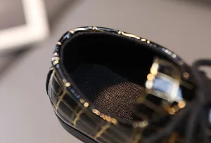 Details der Jungenschuhe mit glänzendem schwarzen Finish und goldenem Karomuster-Dekor