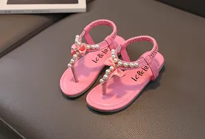 Dettaglio di sandali rosa da bambina con perle finte e fiocco di seta su pelle scura
