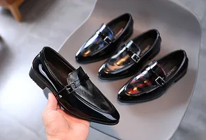 Détail macro du cuir verni noir brillant et de la boucle argentée sur chaussure garçon